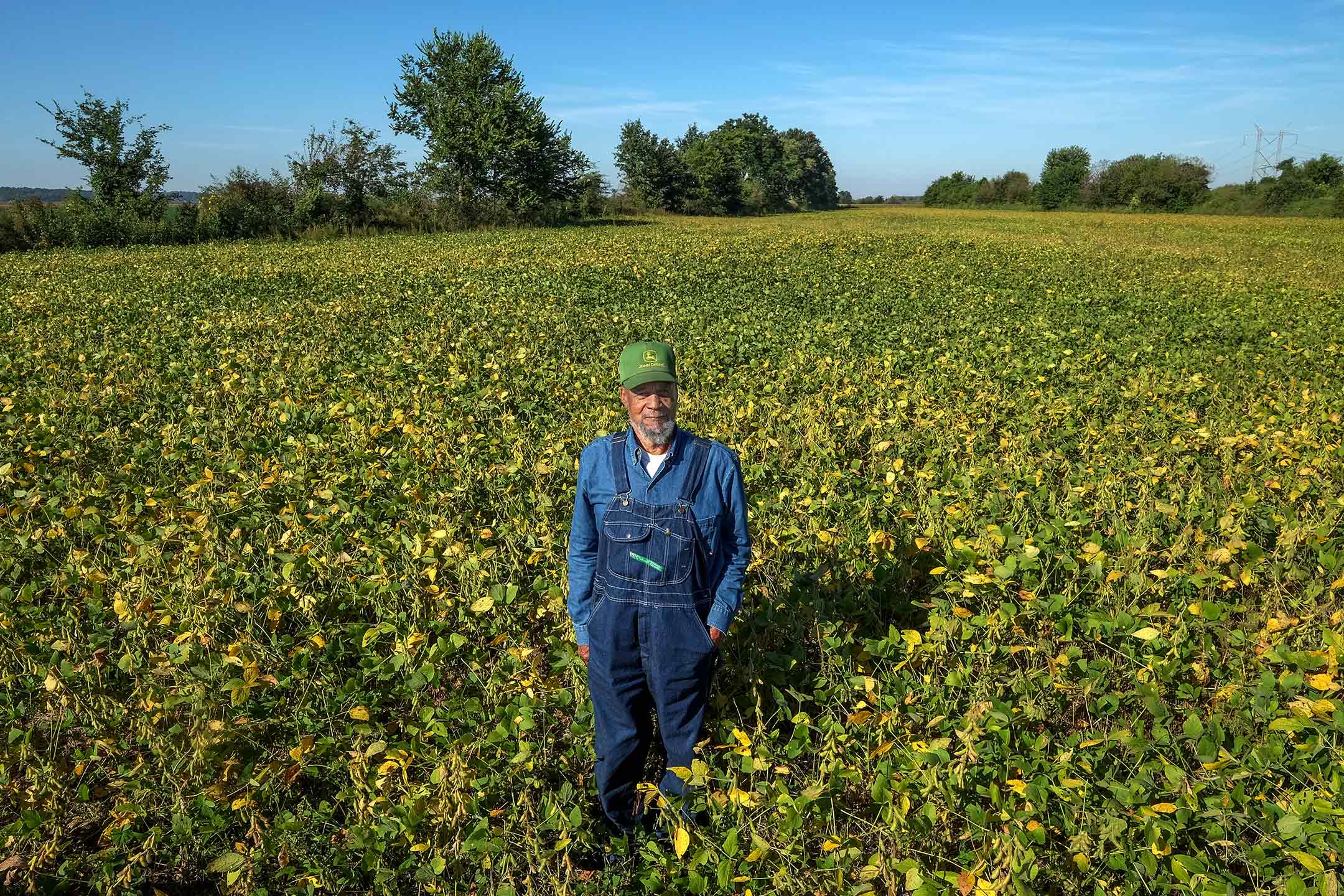 Norman Greer, 79, in jean overhauls and a john deere hat stands in a field of soy beans in the community of Lyles Station in Princeton, IN February 2022.