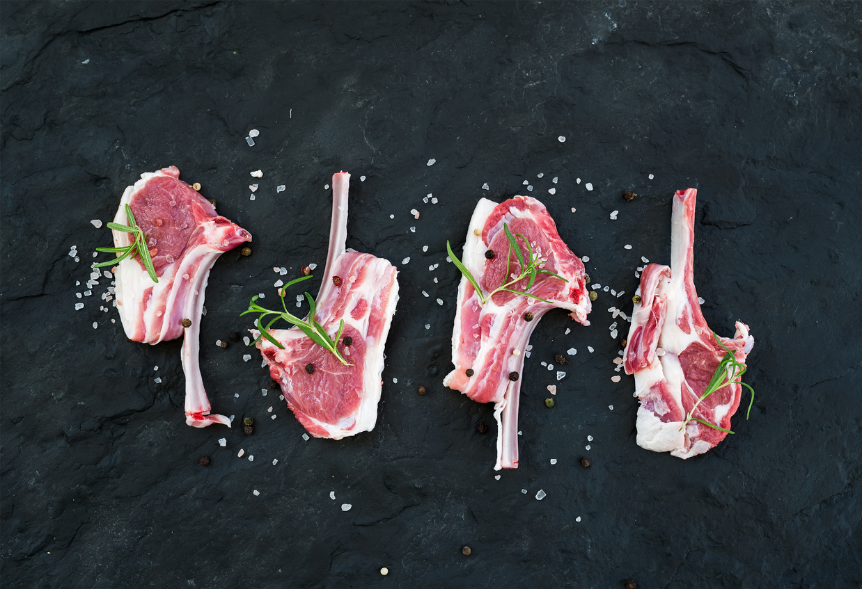 Raw lamb chops with rosemary and spices over dark slate stone background