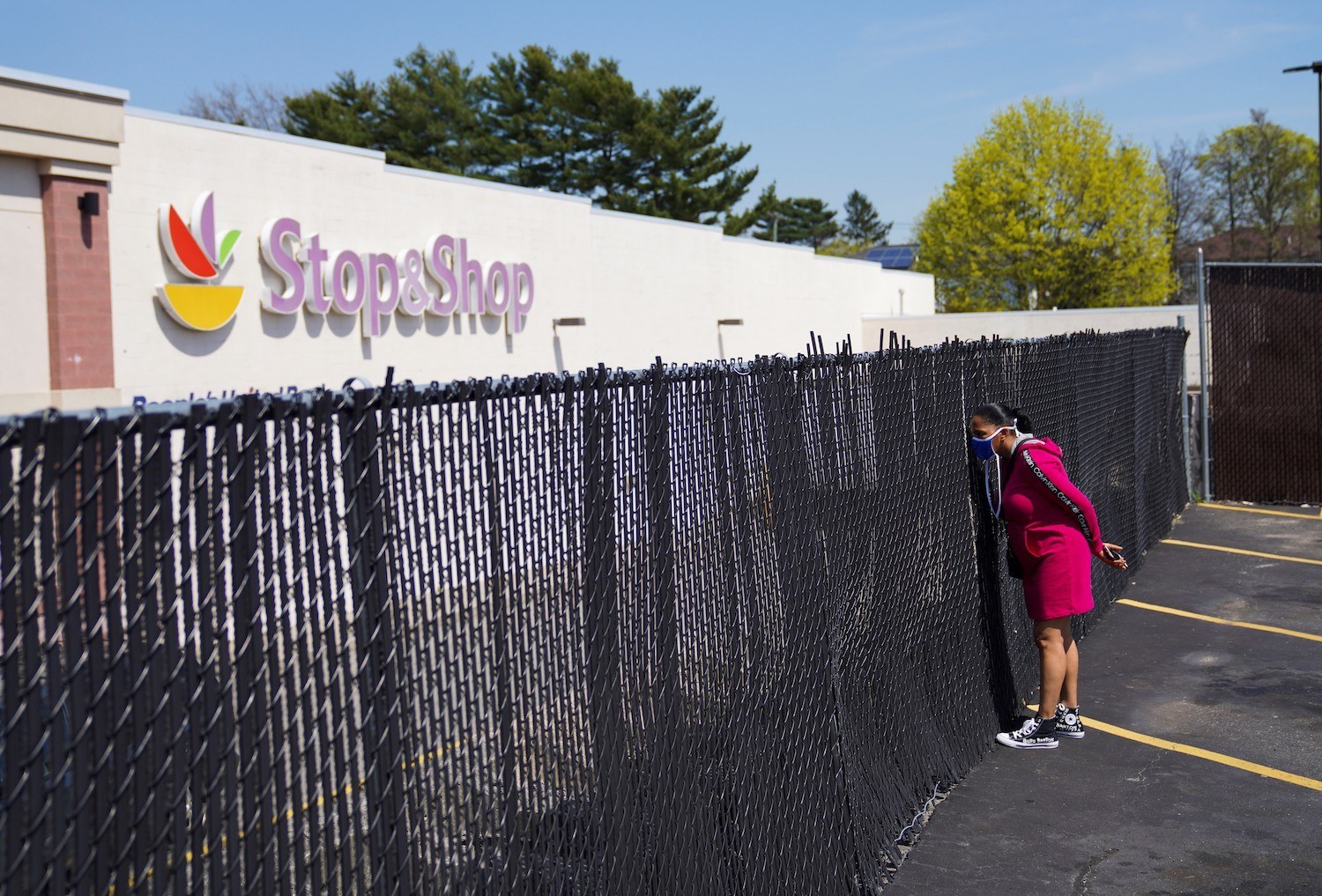 A woman looks through a fence to see a Stop & Shop grocery store in Westhempstead, New York. May 2022
